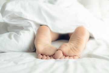 Lifestyle woman feet on the bed under white blanket in the morning. Sleeping and relax Concept