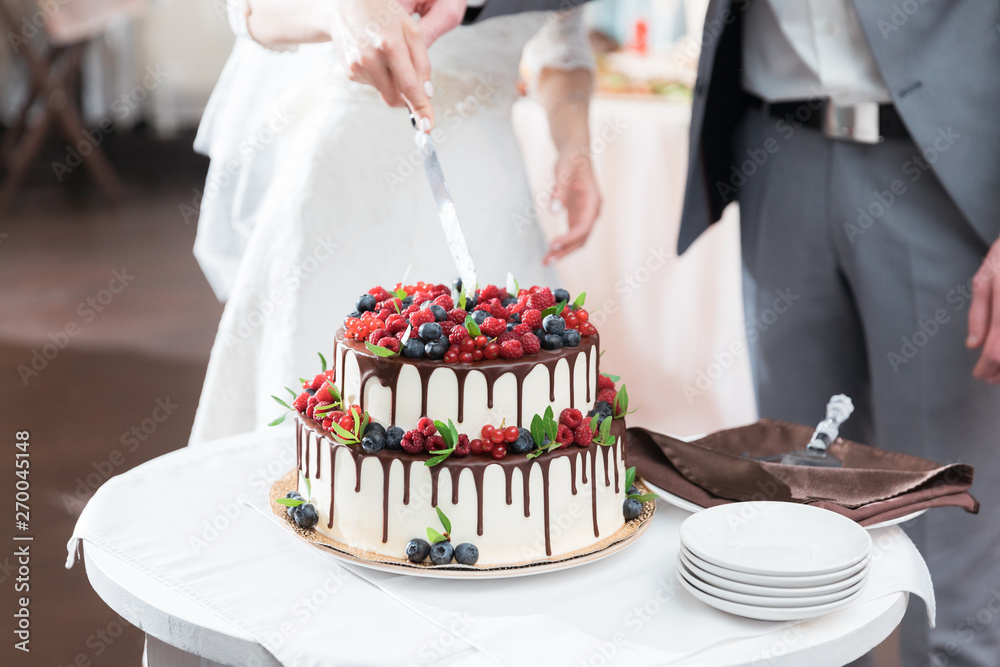 Wall mural bride and groom cut beautiful rustic wedding cake on wedding banquet. the cake is decorated with fre