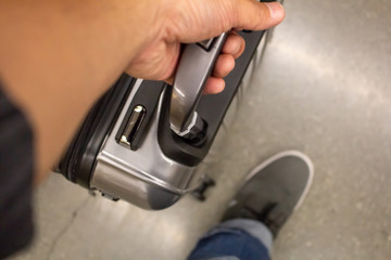 A hand holds onto a rolling compact suitcase at the airport