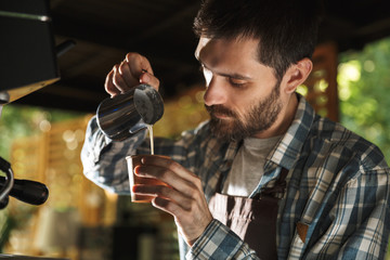 Image of masculine barista man making coffee while working in cafe or coffeehouse outdoor