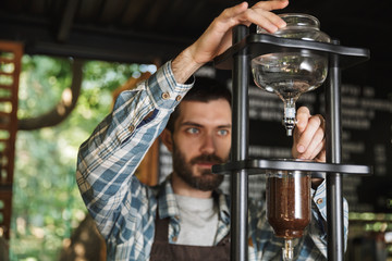 Image of focused barista boy making coffee while working in cafe or coffeehouse outdoor