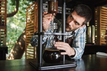 Image of brunette barista boy making coffee while working in cafe or coffeehouse outdoor