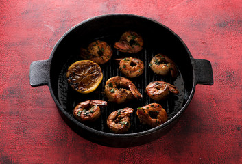 Prawns Shrimps roasted on frying grill pan with lemon  on a red concrete background