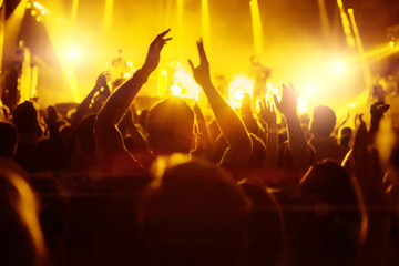 Fototapeta na wymiar Crowd of fans at concert at music festival, silhouettes of raised hands with yellow backlight flare.