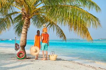 Family on beach, young couple in orange with three year old boy under the palm tree. Summer vacation at Maldives.