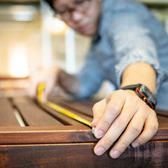 Obraz premium Young Asian man using tape measure for measuring wooden outdoor table in showroom. Shopping furniture for home improvement. Interior design concept