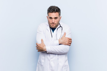 Young handsome doctor man going cold due to low temperature or a sickness.