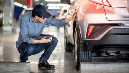Young Asian auto mechanic holding digital tablet checking car wheel in auto service garage. Mechanical maintenance engineer working in automotive industry. Automobile servicing and repair concept