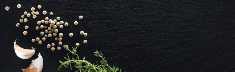 panoramic shot of white pepper on black background near garlic cloves and thyme
