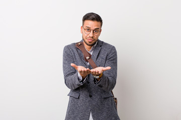 Young business filipino man against a white wall holding something with palms, offering to camera.