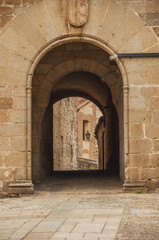Arch gateway passing to an alley between gothic stone buildings in Plasencia