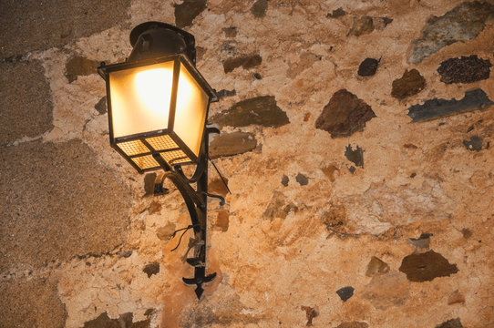 Old Style Metal Sconce Stuck To The Stone Wall And Soft Light At Dusk In Caceres