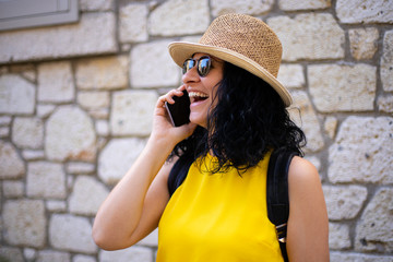 A Cheerful woman is speaking with smartphone in front of a rustic wall