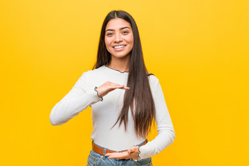 Young pretty arab woman against a yellow background holding something with both hands, product...