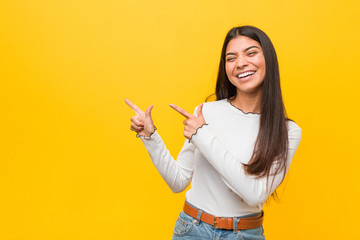 Young pretty arab woman against a yellow background pointing with forefingers to a copy space,...