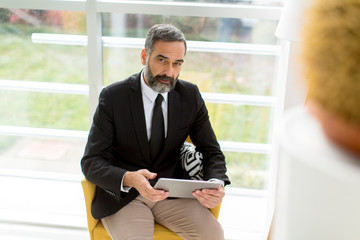 Handsome smiling mature businessman with tablet in the office working, reading or searching something