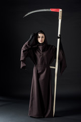 full length view of woman in death costume holding scythe on black