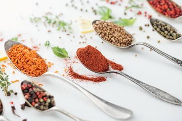 close up view of indian bright spices in silver spoons on white background