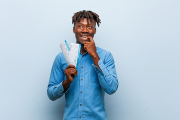 Young rasta black man holding an air tickets relaxed thinking about something looking at a copy space.