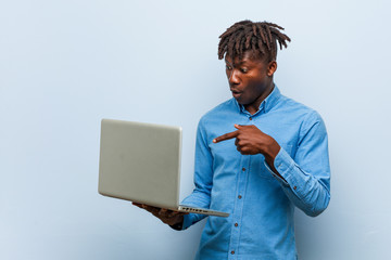 Young rasta black man holding a laptop impressed holding copy space on palm.