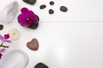 Spa setting with pink orchids, black stones and bath salts on wood background.