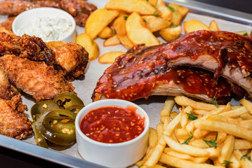 Dish of mixed meats. Grilled ribs, chicken wings and sausages with French fries