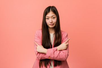 Obraz premium Young business chinese woman wearing pink suit points sideways, is trying to choose between two options.