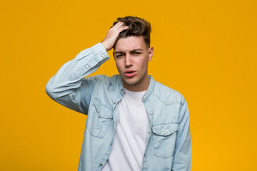 Young handsome student wearing a denim shirt tired and very sleepy keeping hand on his head.