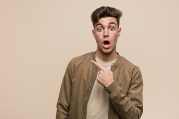 Young caucasian man wearing a brown jacket pointing to the side