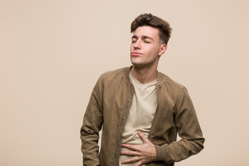 Obraz premium Young caucasian man wearing a brown jacket touches tummy, smiles gently, eating and satisfaction concept.