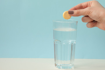Glass with water on a white background with effervescent tablets vitamins. Vitamin C over blue background