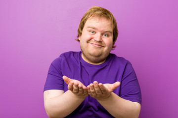 Young authentic redhead fat man holding something with palms, offering to camera.