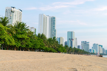 Fototapeta na wymiar Green tropical trees on beach with tall hotels and clear sand