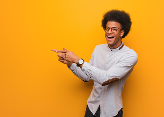 Young african american man over an orange wall pointing to the side with finger