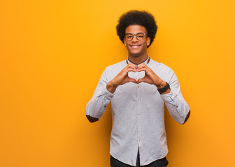 Young african american man over an orange wall doing a heart shape with hands