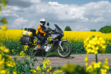 Fototapeta na wymiar Girl in a protection outfit and glasses with touristic motorcycle. Rape yellow flowers field on background. Adventure trail tour, enduro and off road, summer day. extreme vacation concept