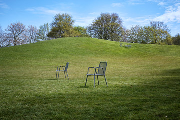 Zwei Stühle stehen auf einer Wiese im Park, im Hintergrund eine Liege auf einem Hügel