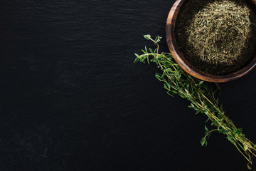 top view of thyme spice in wooden bowl near green herb on black background