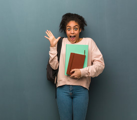 Young student black woman celebrating a victory or success. She is holding books.