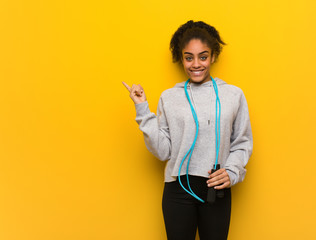 Young fitness black woman pointing to the side with finger. Holding a jump rope.