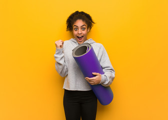 Young fitness black woman screaming very angry and aggressive. Holding a mat.