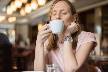 Young woman enjoying in a cup of coffee while sitting in a bar