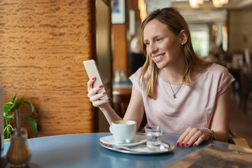 Happy woman reading text message on cell phone in cafe