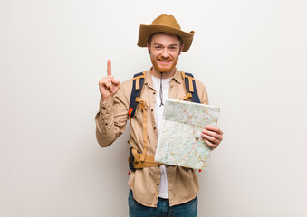Young redhead explorer man showing number one. Holding a map.