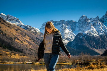 Naklejka premium Beautiful young russian woman in front of autumn landscape with mountain lake Tumanly-kel, the Mist lake, located in Russia, near Dombay , in Caucasus mountains, Gonachkhir gorge