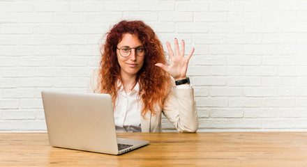 Young redhead curly woman working with her laptop smiling cheerful showing number five with fingers.