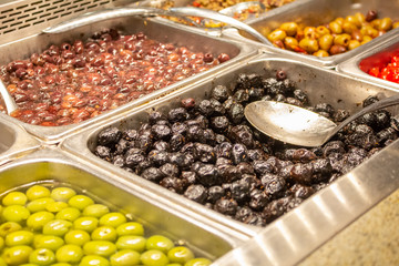 Several varieties of olives at the olive bar of a grocery store