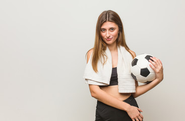 Young fitness russian woman crossing arms, smiling and relaxed. Holding a soccer ball.