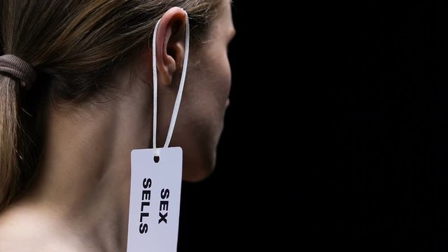 Man hand hanging sex sells label on lady ear, forced prostitution discrimination