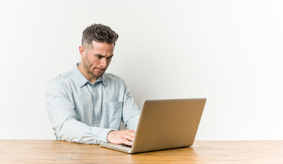 Young handsome man working with his laptop confused, feels doubtful and unsure.